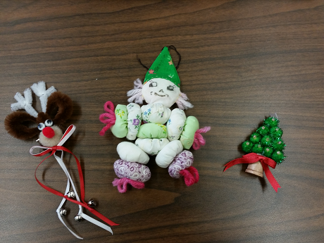 Holiday ornaments that include a pipe cleaner reindeer, cloth clown, and pompom tree
