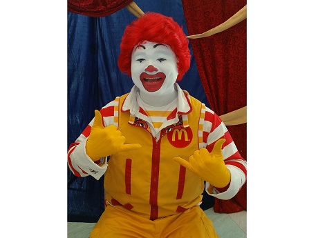 Ronald McDonald sitting with shaka hand gestures