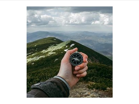 photo of hand holding wrist compass overlooking mountain terrain