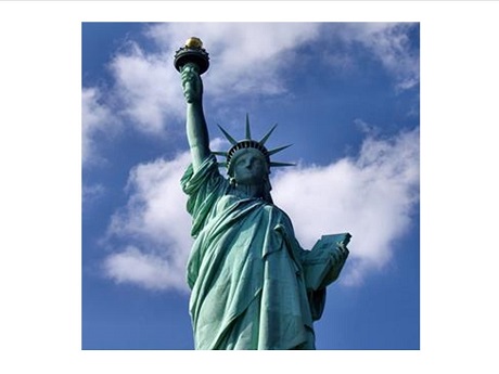 Photo of Statue of Liberty from waist up against a blue sky with white clouds.