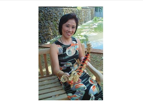Photo of Barbara Chung Ho seated holding a piece of traditional Chinese knotting artwork.