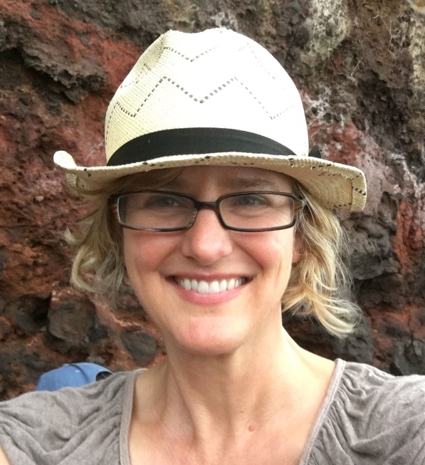 Annie with a hat with rectangular frames and a beige colored straw hat in front of a rock formation