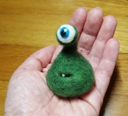 one eyed green felt alien held in hand