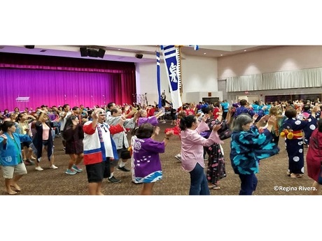 People of all ages dancing indoors doing bon dance.