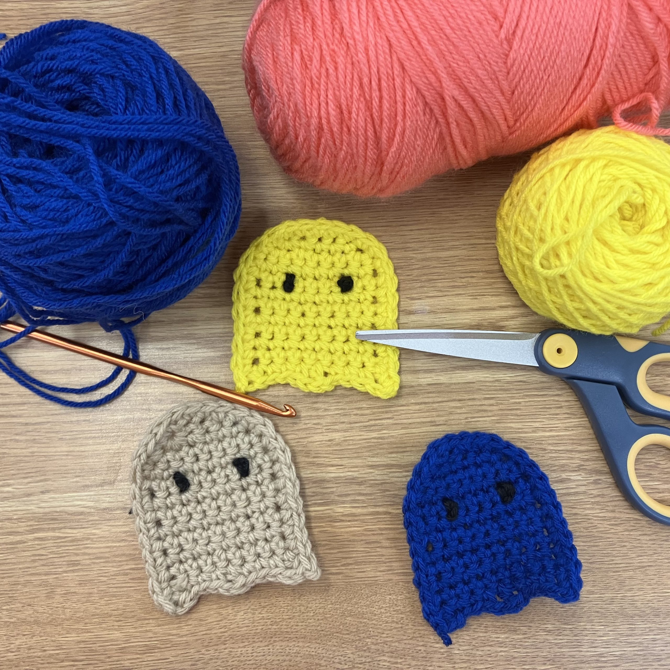 crocheted flat ghosts in various colors surrounded by yarn, scissor, and crochet hook