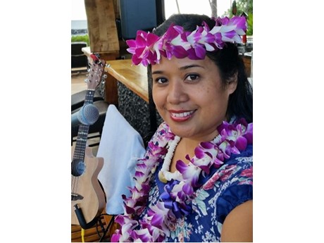 A person wearing a flower lei and sitting in front of a guitar