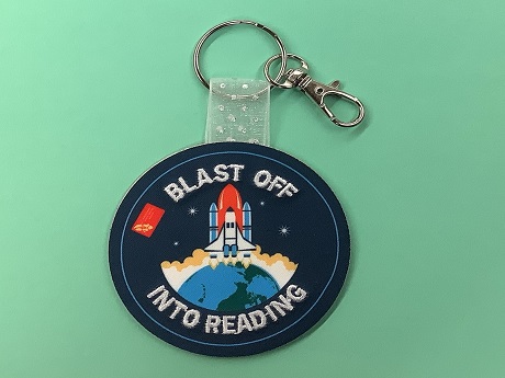 Keychain with a spaceship taking off over Earth that reads "Blast Off Into Reading"