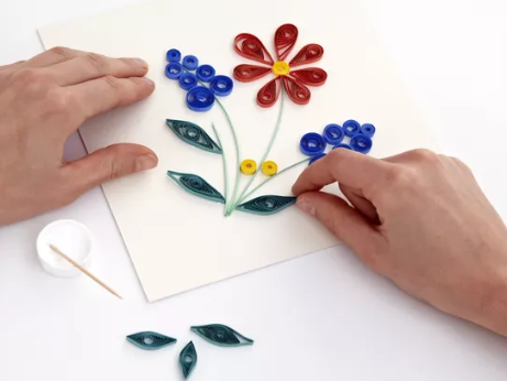 Two hands making a bunch of blue and red flowers out of rolled strips of colored paper.