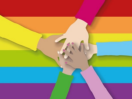 Five hands together over a rainbow pride flag.